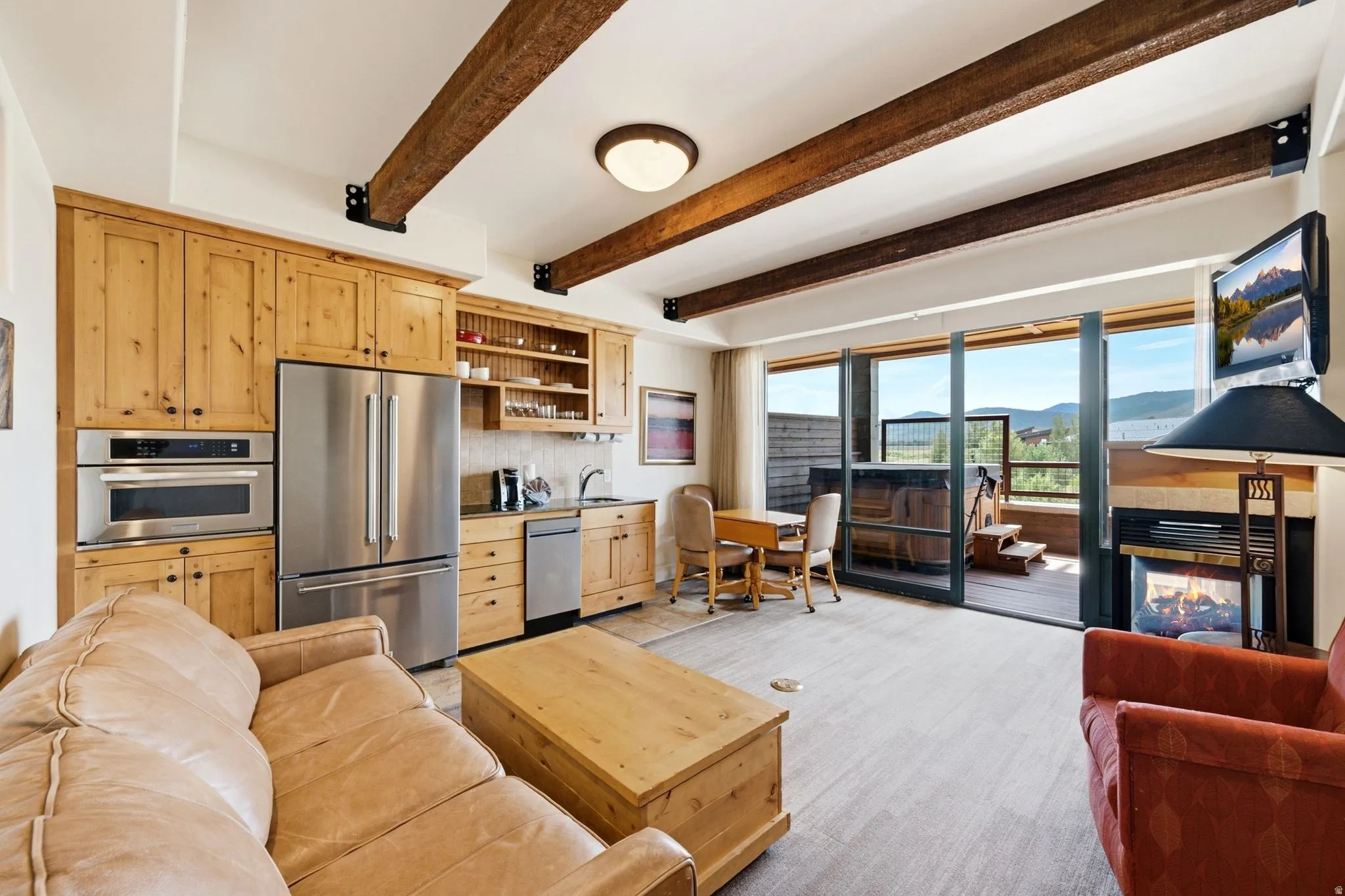Exposed ceiling beams, full-height glass doors, a built-in fireplace, a built-in microwave, and a stainless steel refrigerator