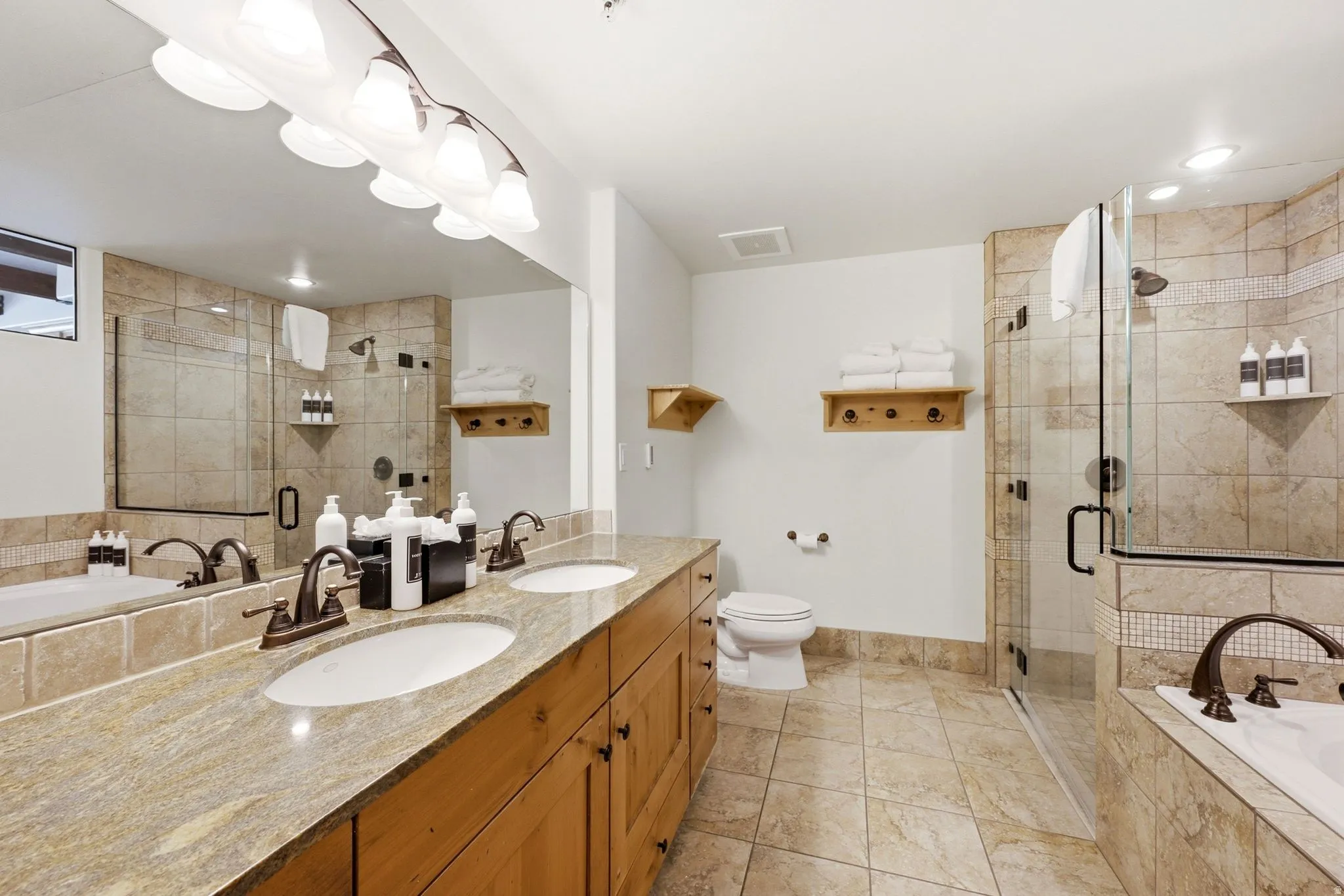 Dual vanity with light-toned countertop, wood-finish cabinetry, and bronze-finish fixtures