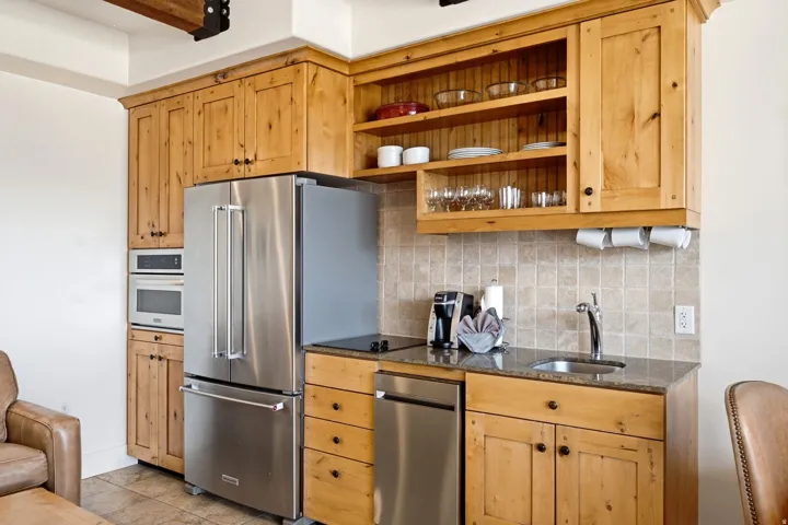 Stainless steel appliances, wood cabinetry, granite-style countertops, tile flooring, and a tile backsplash