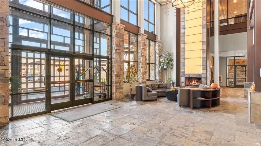 Grand entrance with expansive window walls, stone-clad columns, a floor-to-ceiling fireplace, and large format stone flooring