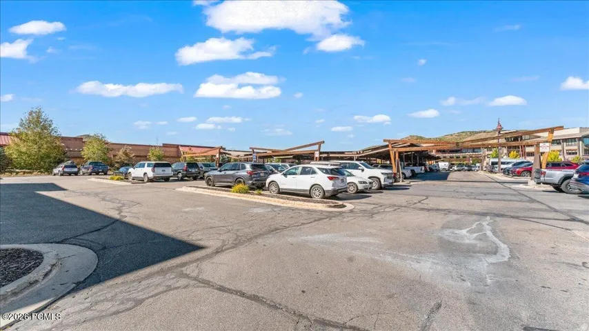 Paved parking lot with designated parking spaces, wood-frame shade structures, and an array of commercial buildings