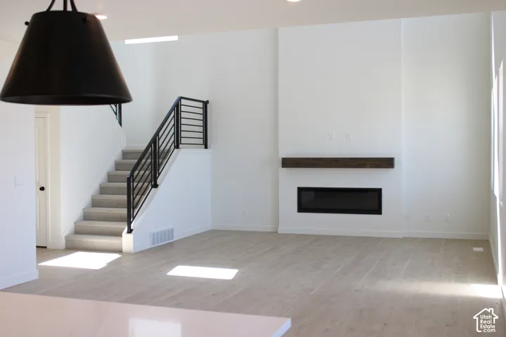 Contemporary linear fireplace with a substantial wood mantel, sleek black metal stair railing, light wood-finish flooring, and recessed ceiling lighting