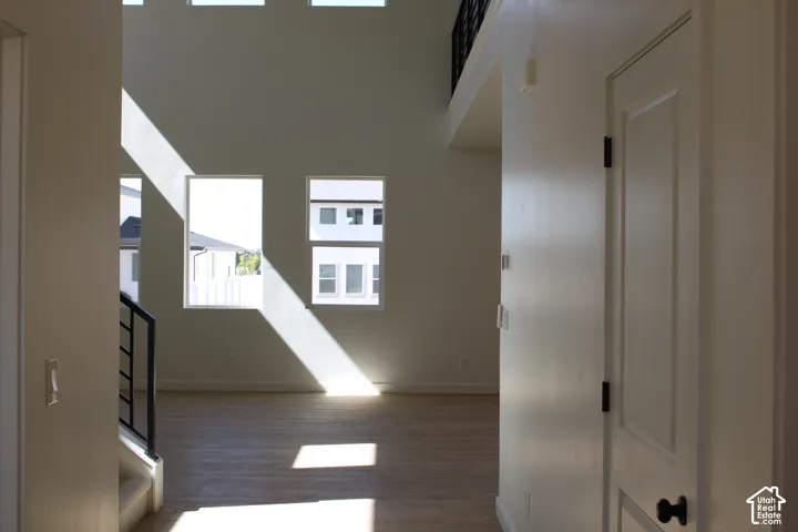 Two-story ceiling, multiple windows, wood-finish flooring, white paneled door, black metal stair railing