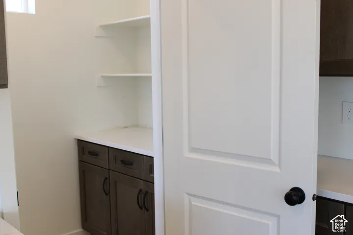 Pantry featuring white shelving, lower cabinetry with dark hardware, and a light-colored countertop