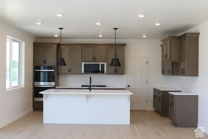 Kitchen featuring a center island, recessed lighting, double wall ovens, wood-finish flooring, and pendant lighting