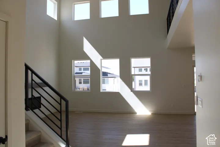 Soaring ceiling height with multiple upper windows, wood-finish flooring, and a contemporary black metal stair railing