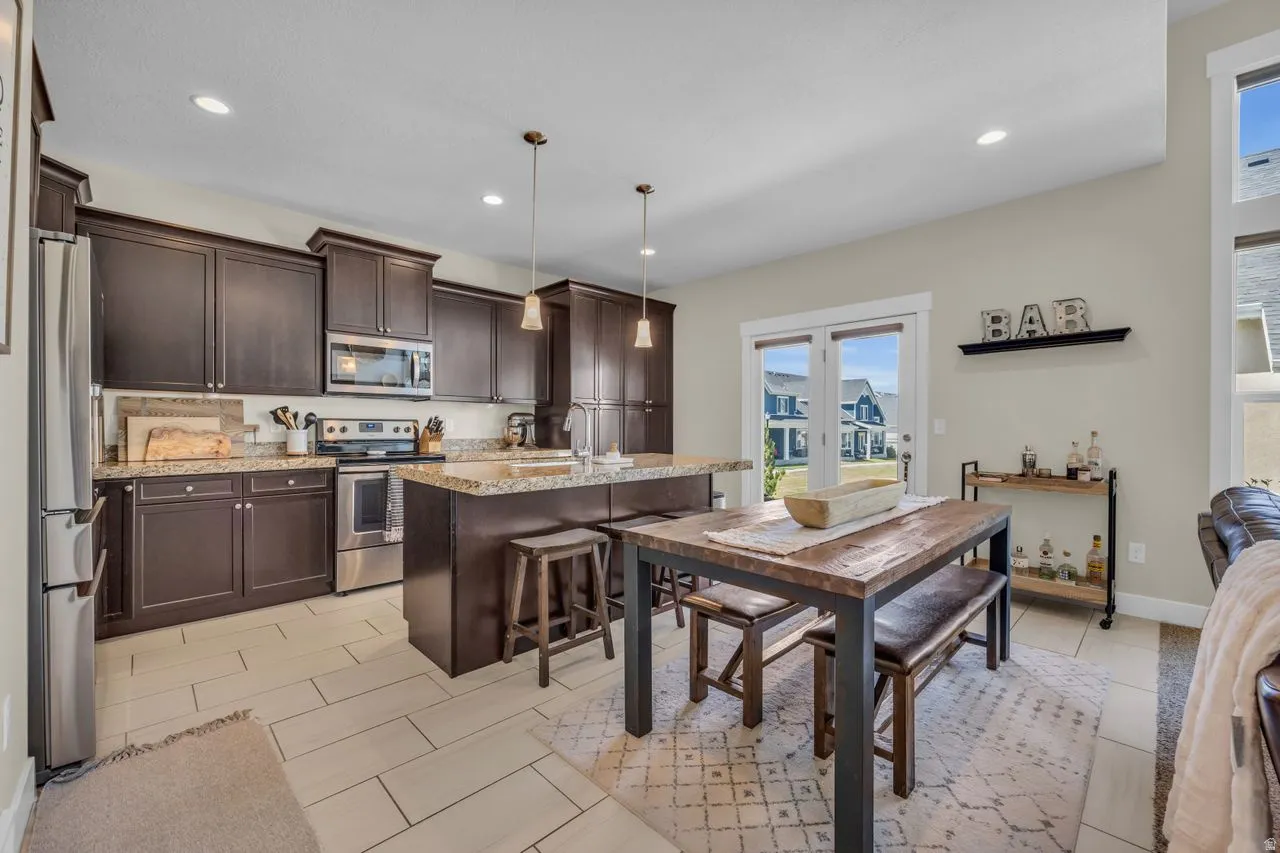 Kitchen with dark wood cabinetry, stainless steel appliances, granite countertops, a central island, and tile flooring