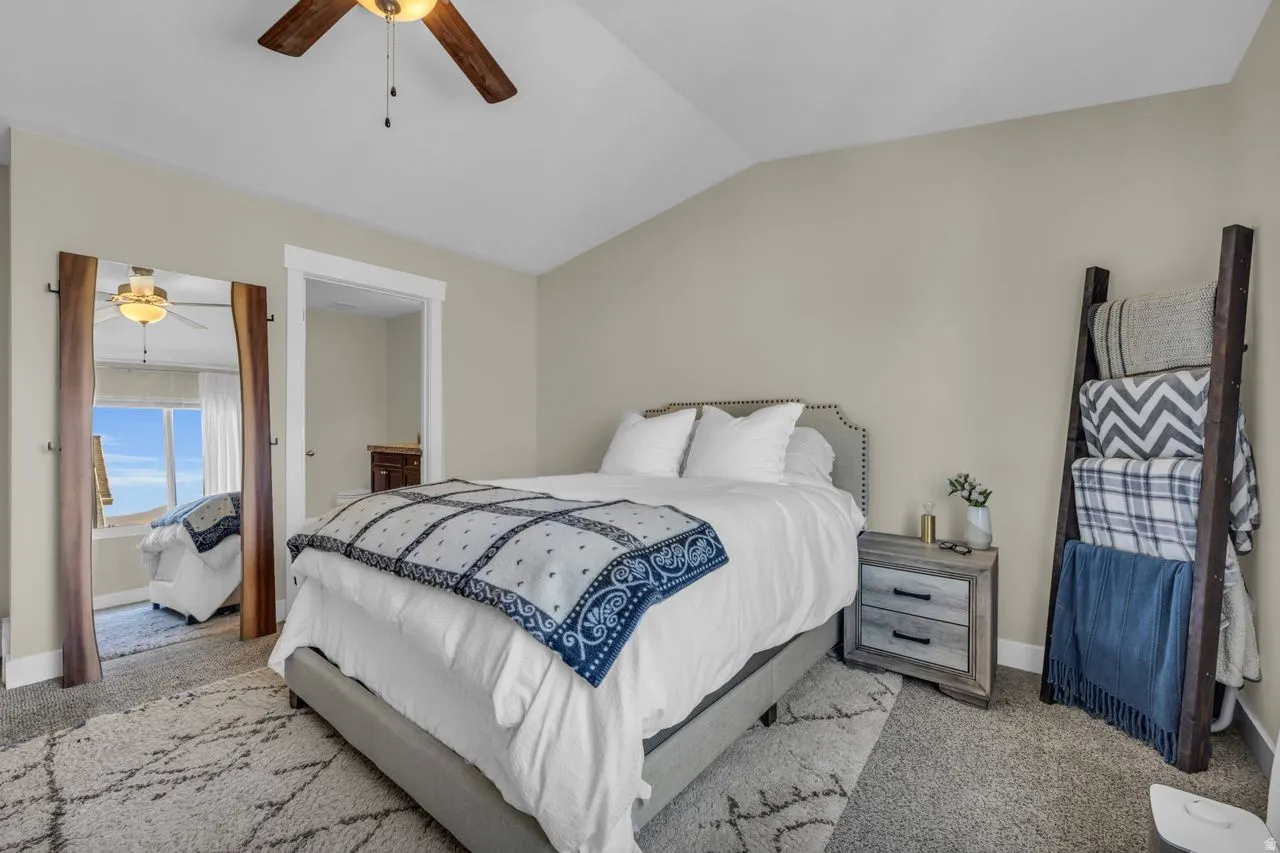 Vaulted ceiling with a wood-finish ceiling fan, neutral wall color, and carpet flooring