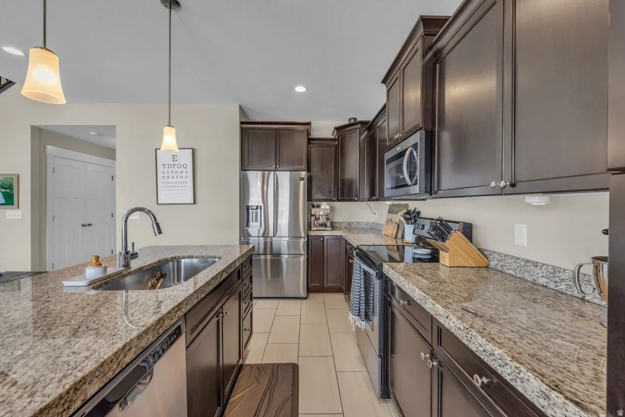 Well-appointed kitchen featuring dark wood cabinetry, light-toned countertops, stainless steel appliances, and tile flooring