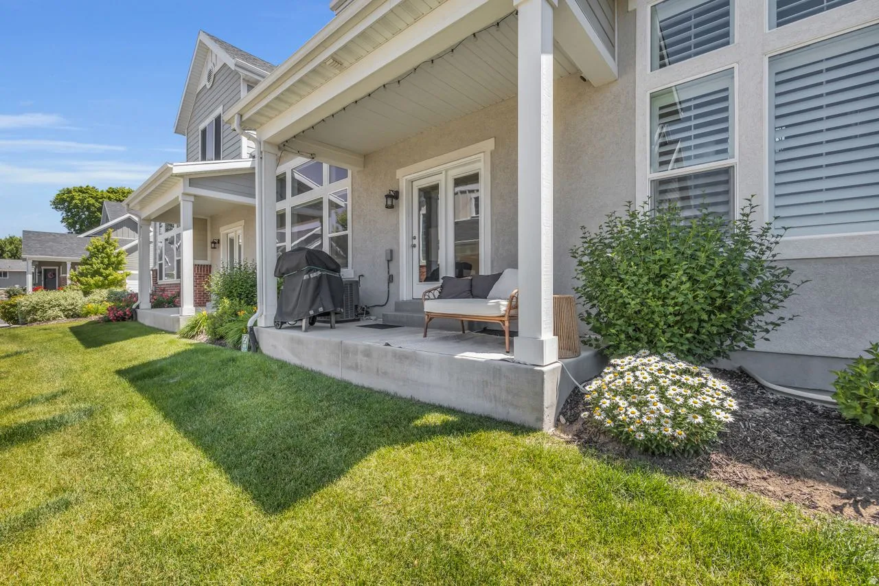 Rear concrete patio featuring a stucco exterior and multiple windows with horizontal blinds