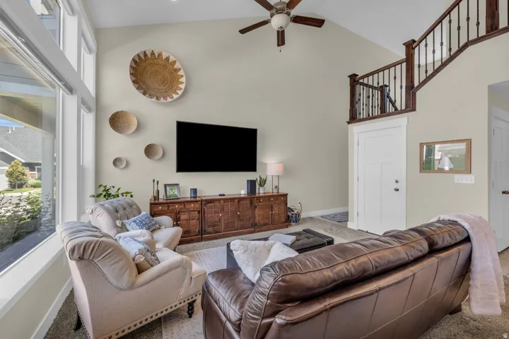Vaulted ceiling with an attached ceiling fan, large windows, wood media console, and a staircase with dark wood railings
