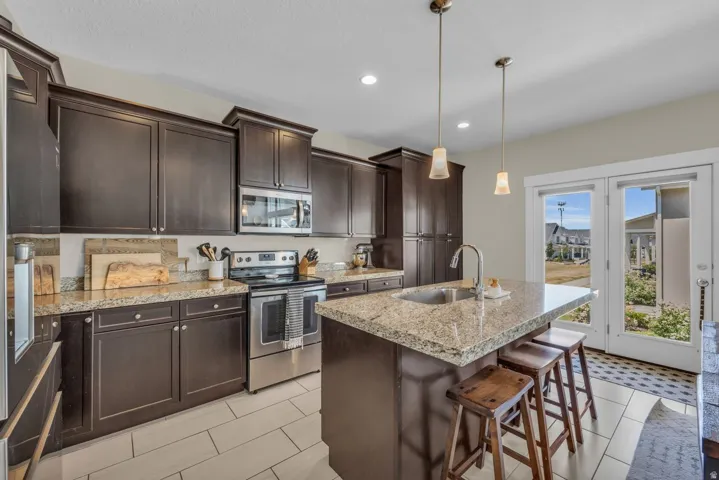 Kitchen featuring dark wood cabinetry, stainless steel appliances, granite countertops, and a center island with a sink