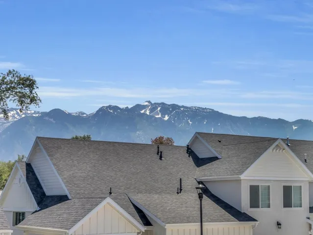 Snow-capped mountains create a dramatic backdrop for this property, featuring a durable shingle roof and white siding