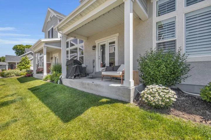 Rear concrete patio featuring a stucco exterior and multiple windows with horizontal blinds