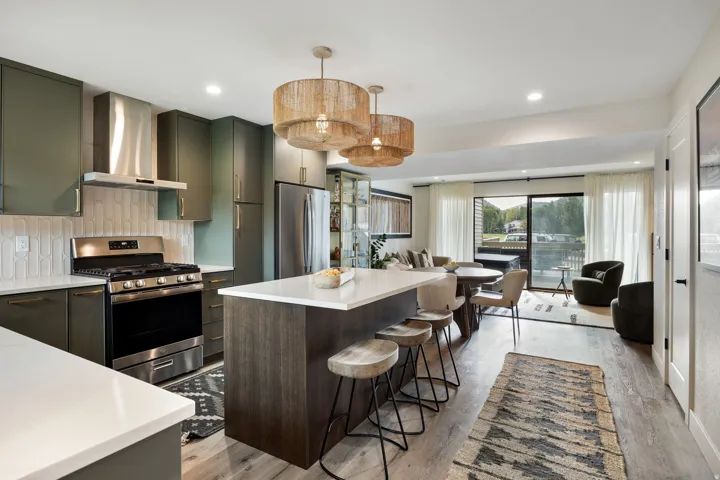 Modern kitchen featuring matte green cabinetry, stainless steel appliances, a white tile backsplash, and a wood-finish island with white countertops