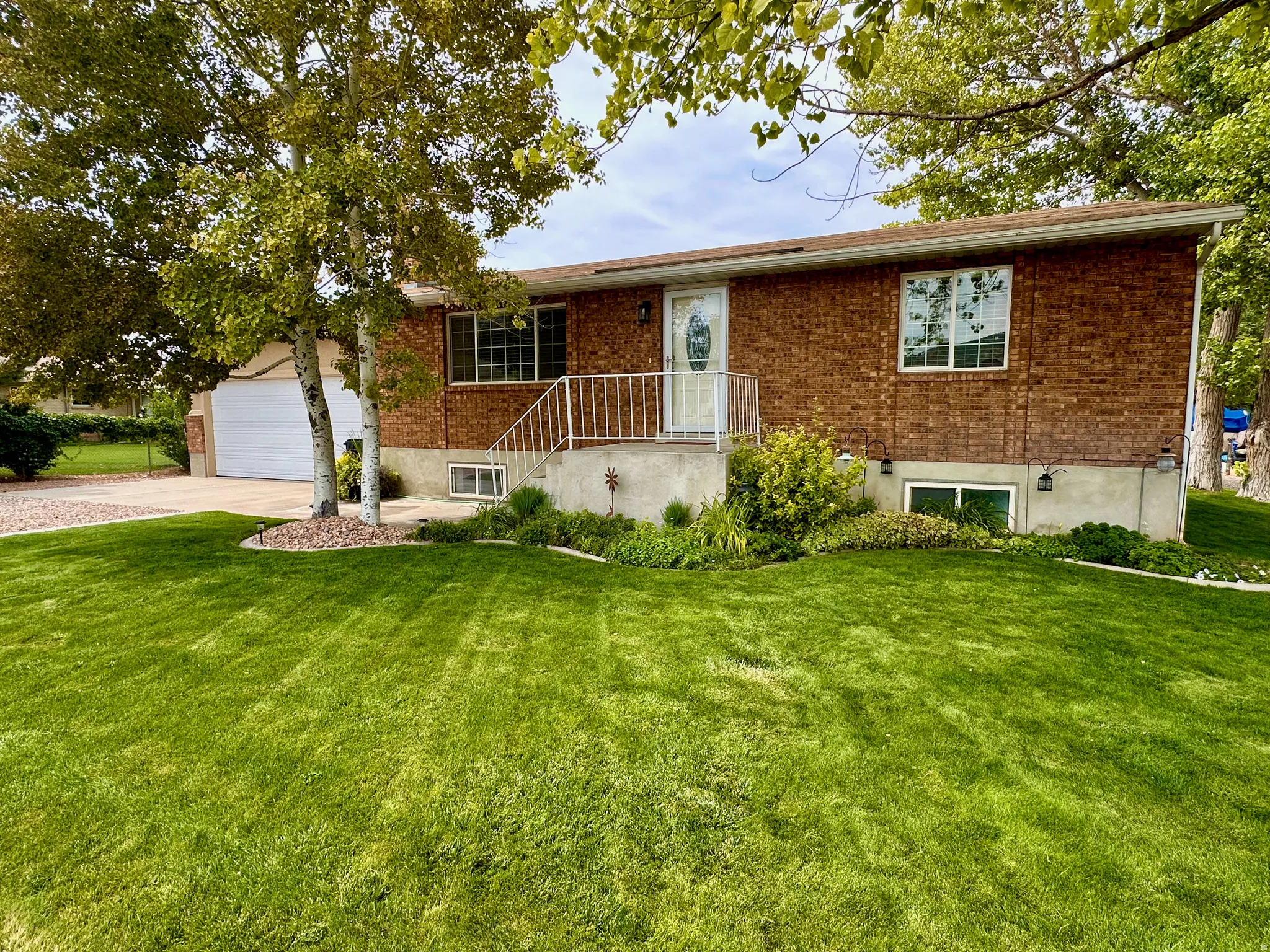Brick exterior featuring an attached two-car garage, front entry with white railing, and established landscaping