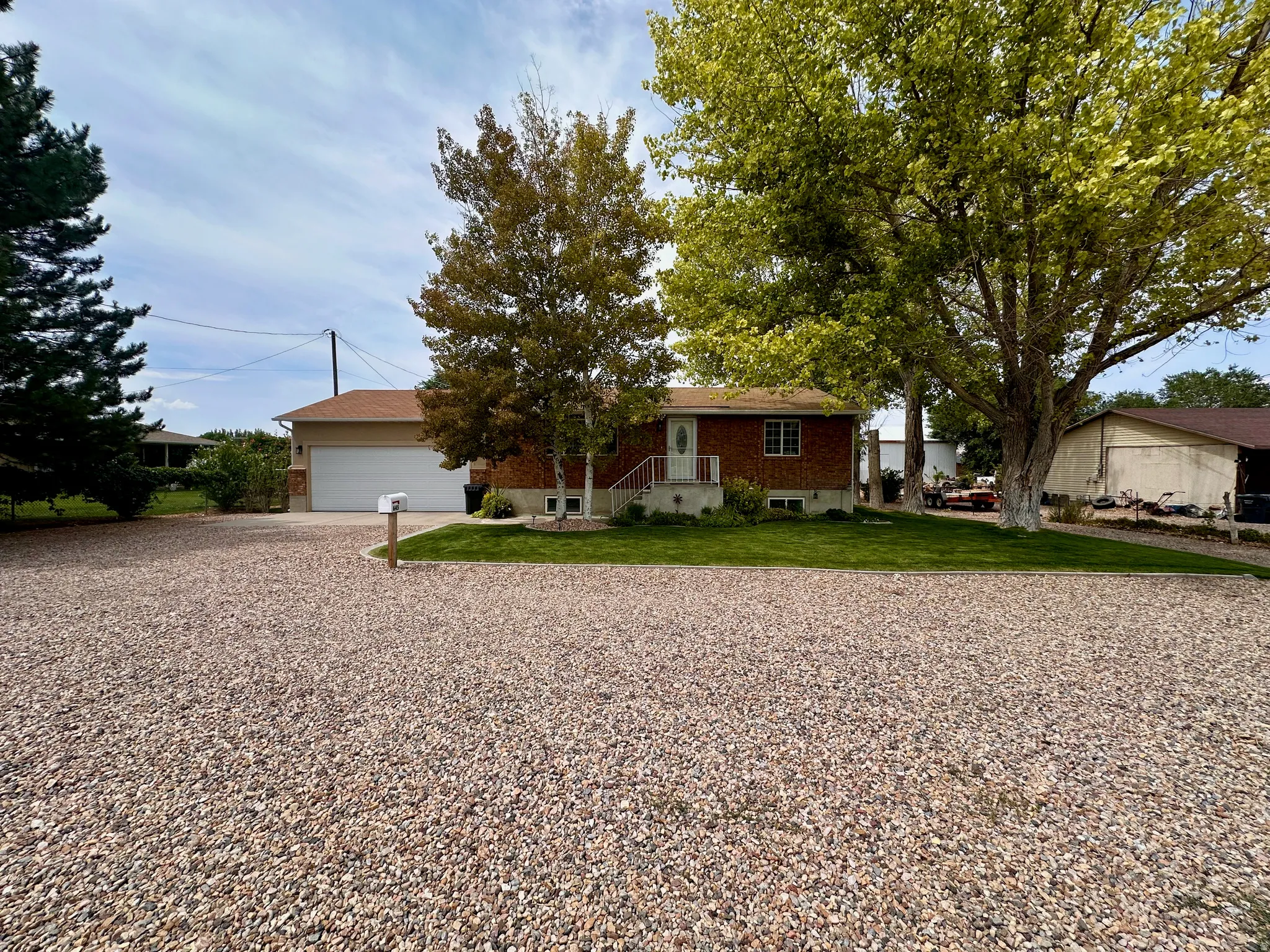 Brick facade, white garage door, gravel driveway, mature trees, manicured lawn