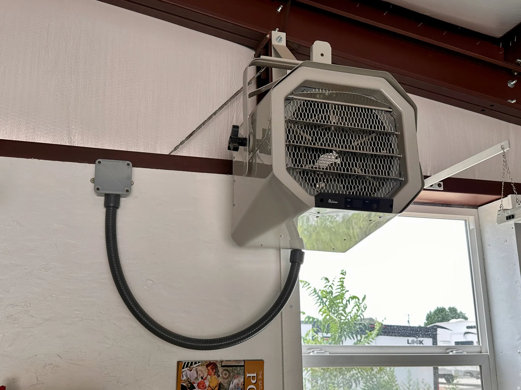 Wall-mounted heating unit with a metal grille, suspended from exposed structural beams, featuring a lower window with a white frame