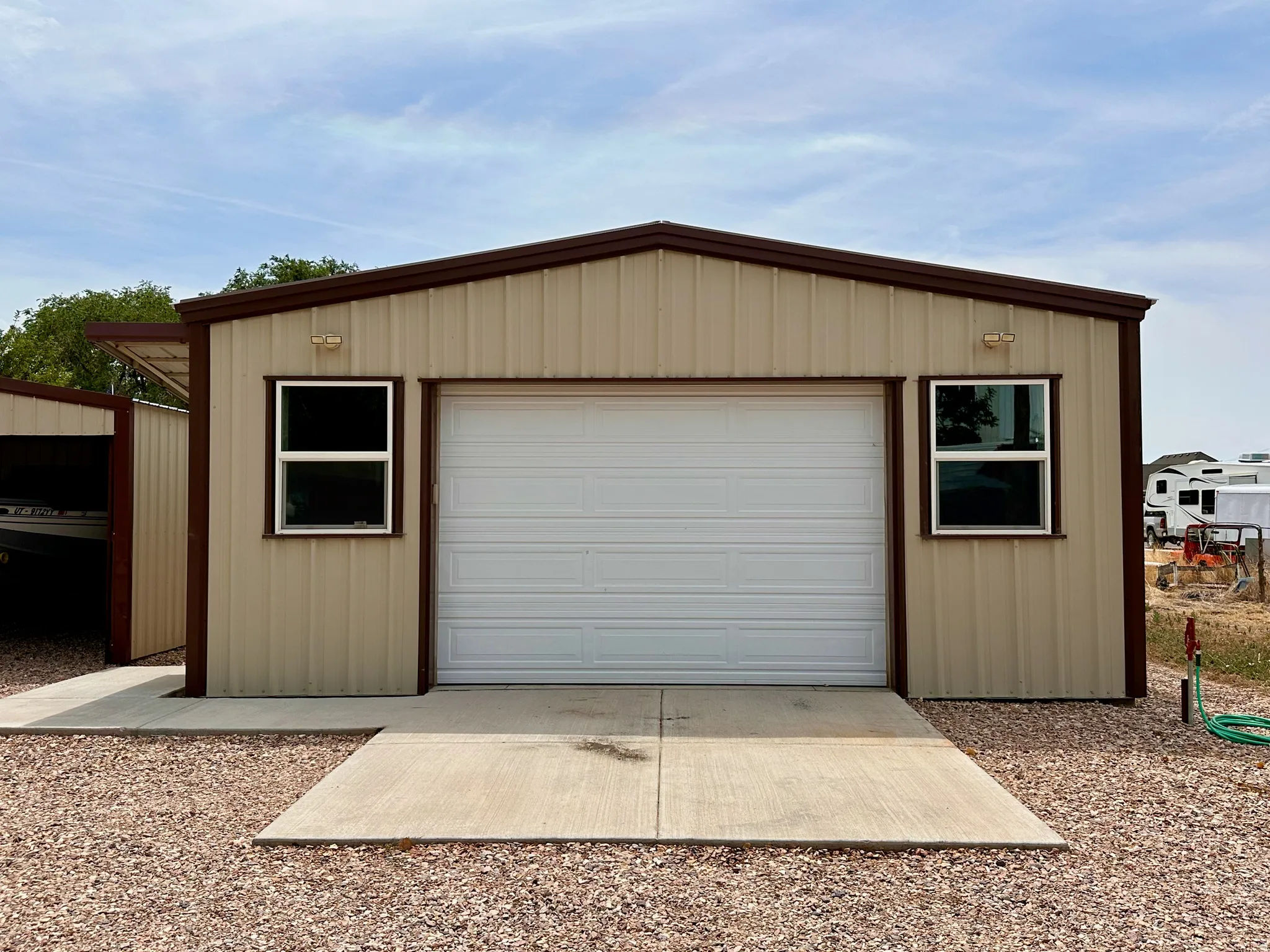 Metal-clad structure with a pitched roof, a white garage door, two windows, and concrete pad