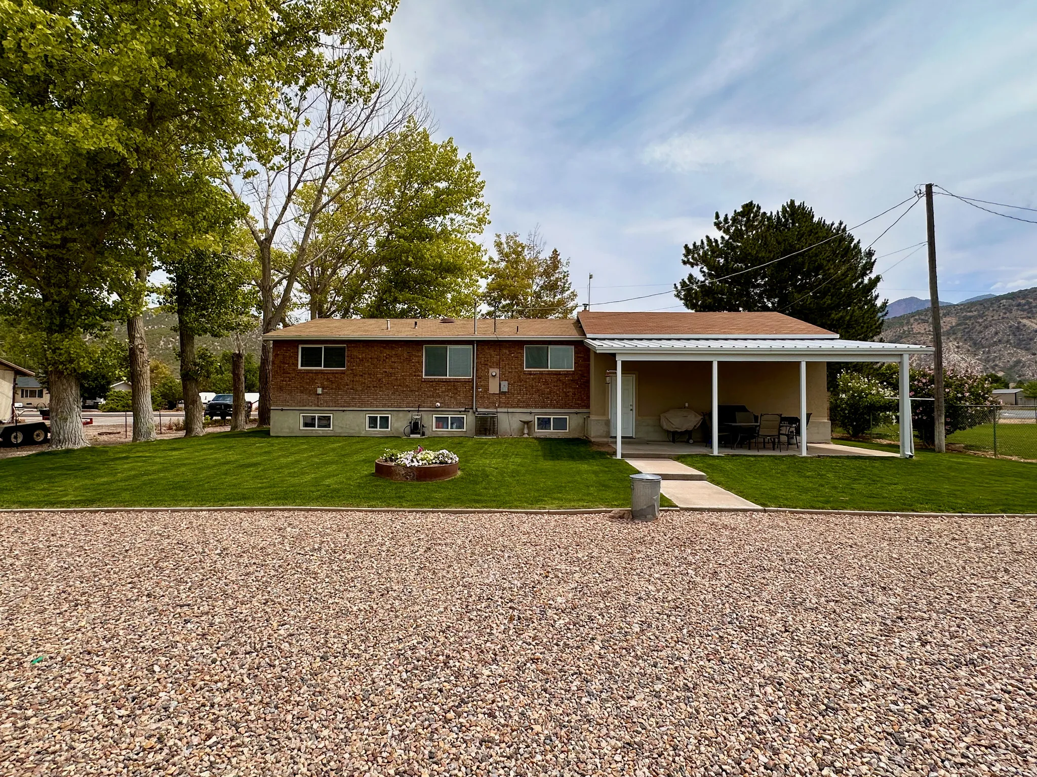 Brick exterior with a covered patio, expansive lawn, and mature trees