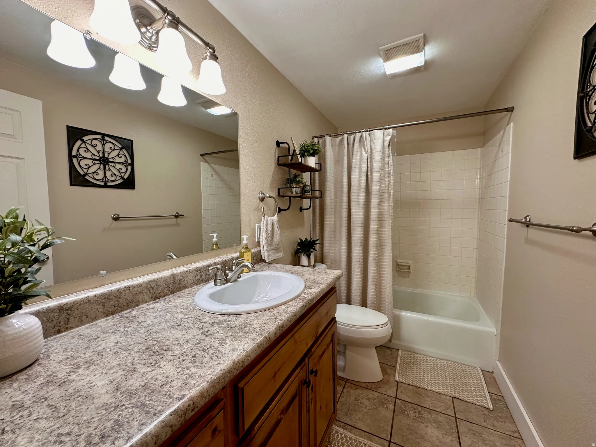 Spacious vanity with an integrated sink and wood-finish cabinetry, tile flooring, and a tiled shower-over-tub