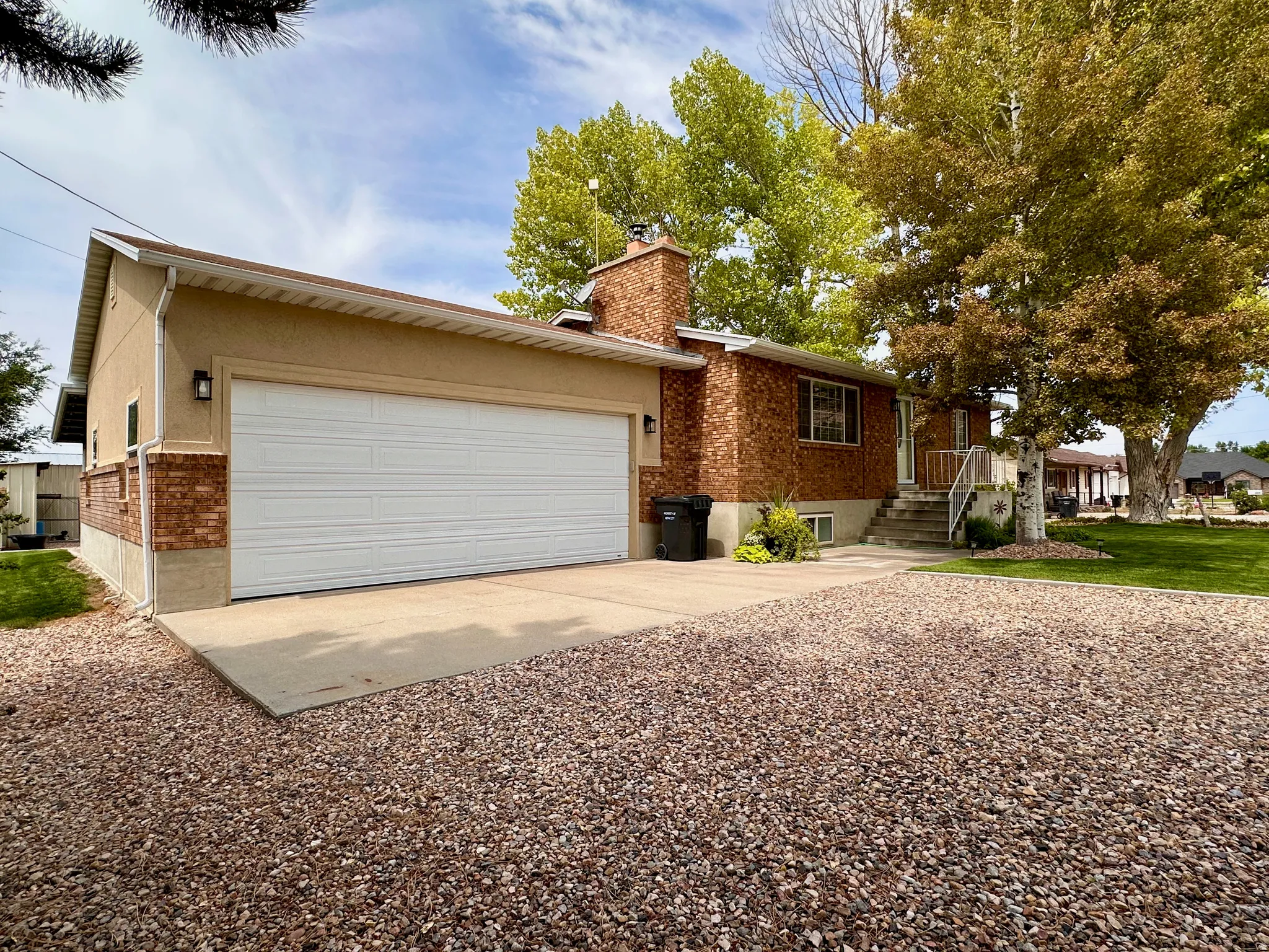 Brick and stucco exterior, attached garage, concrete driveway, gravel landscaping, mature trees