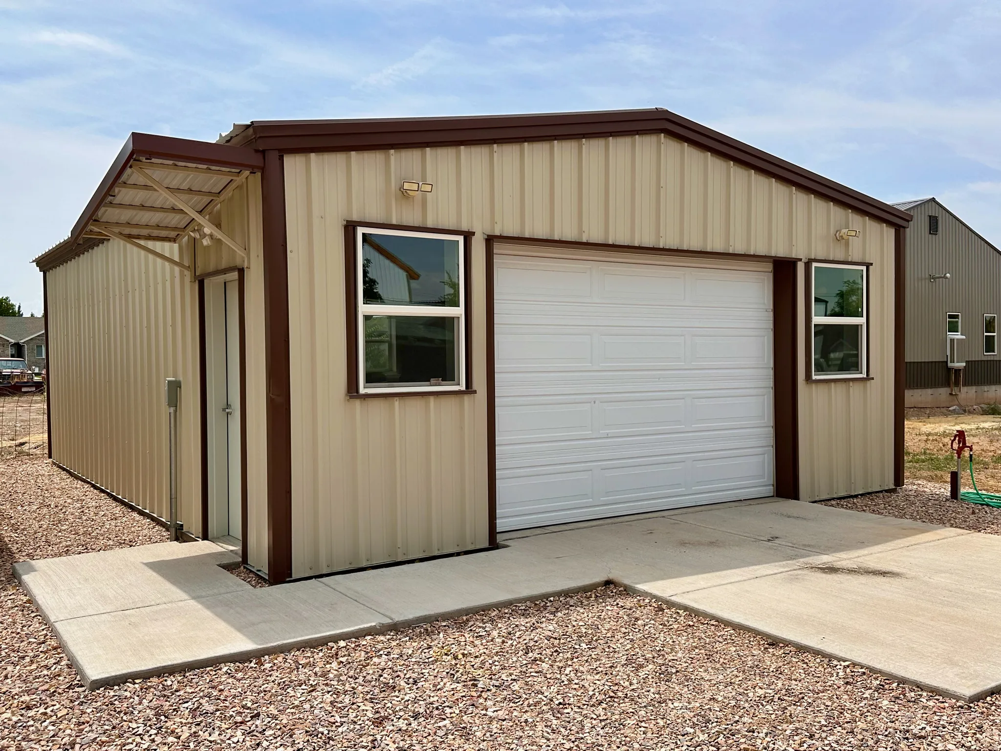 Metal-sided structure with a single garage door, two windows, and an awning over a side entrance