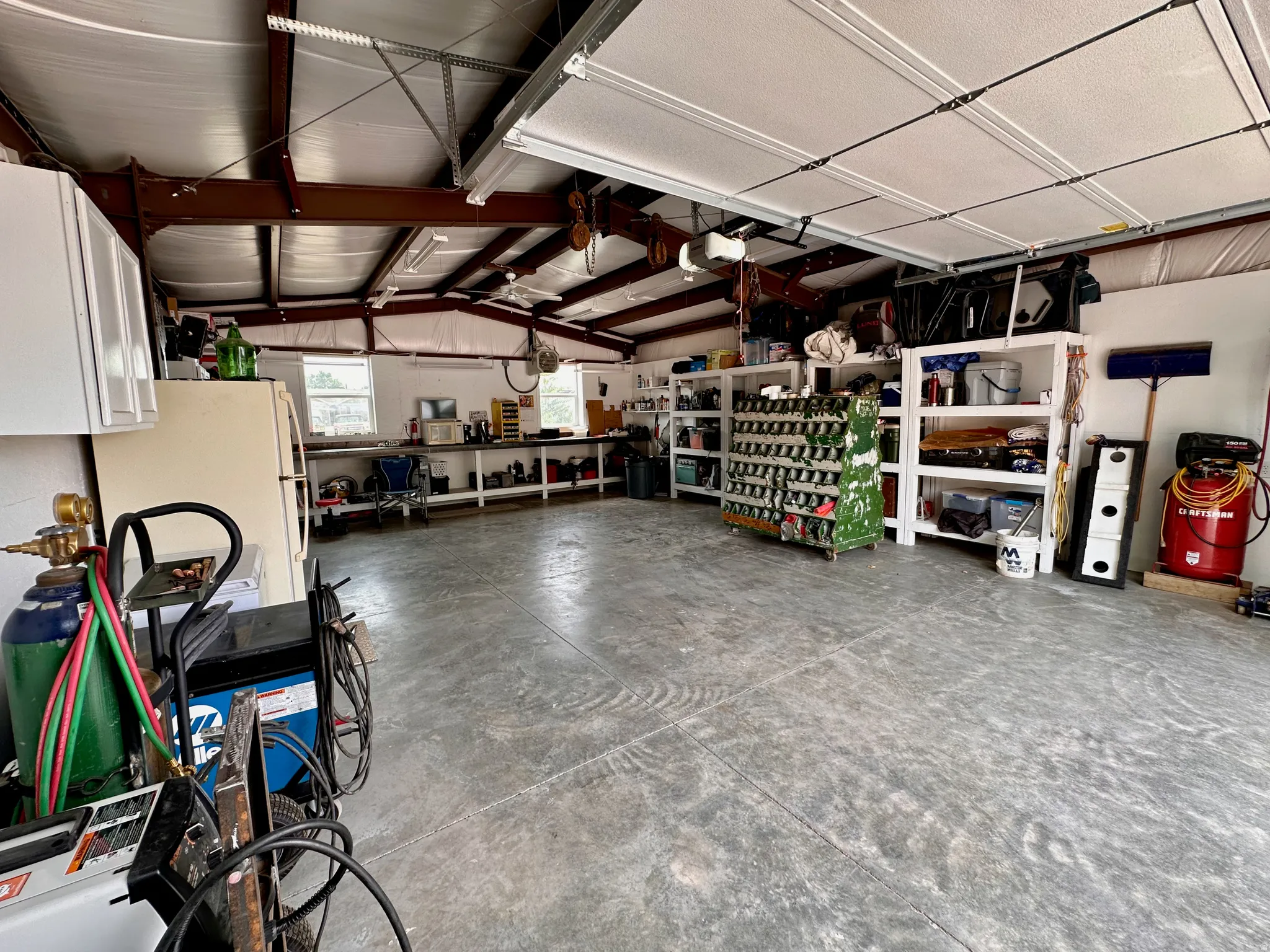 Spacious garage with exposed beam ceiling, multiple windows, and extensive built-in shelving