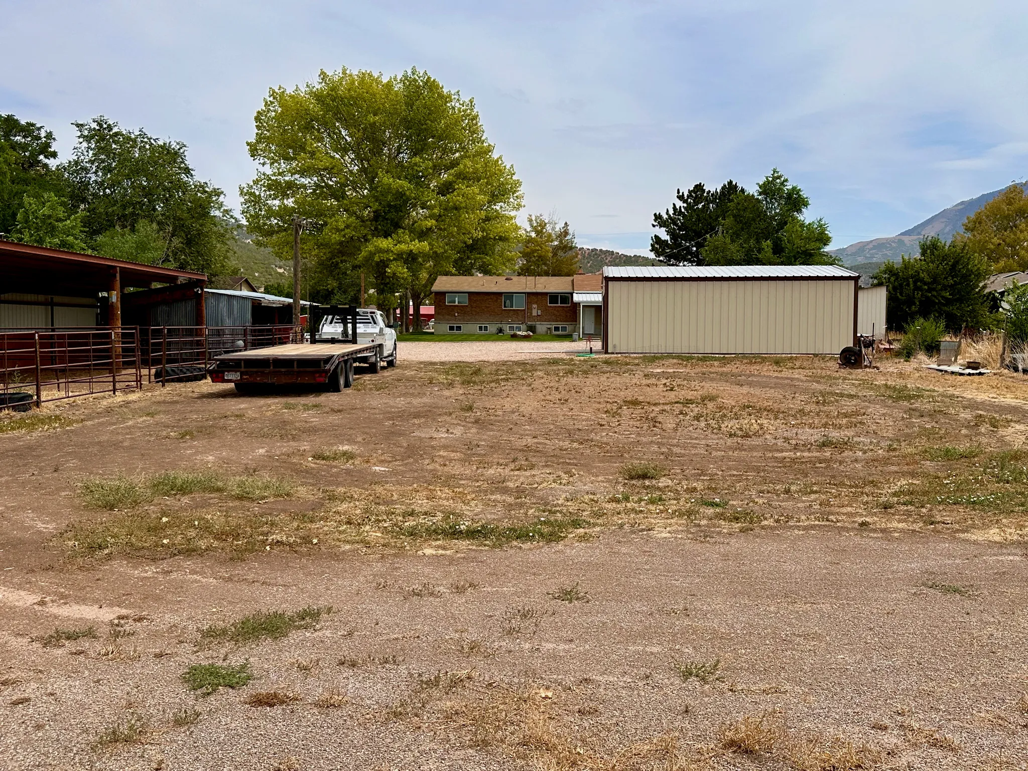 Large gravel lot with a metal-sided outbuilding and a red-roofed covered structure