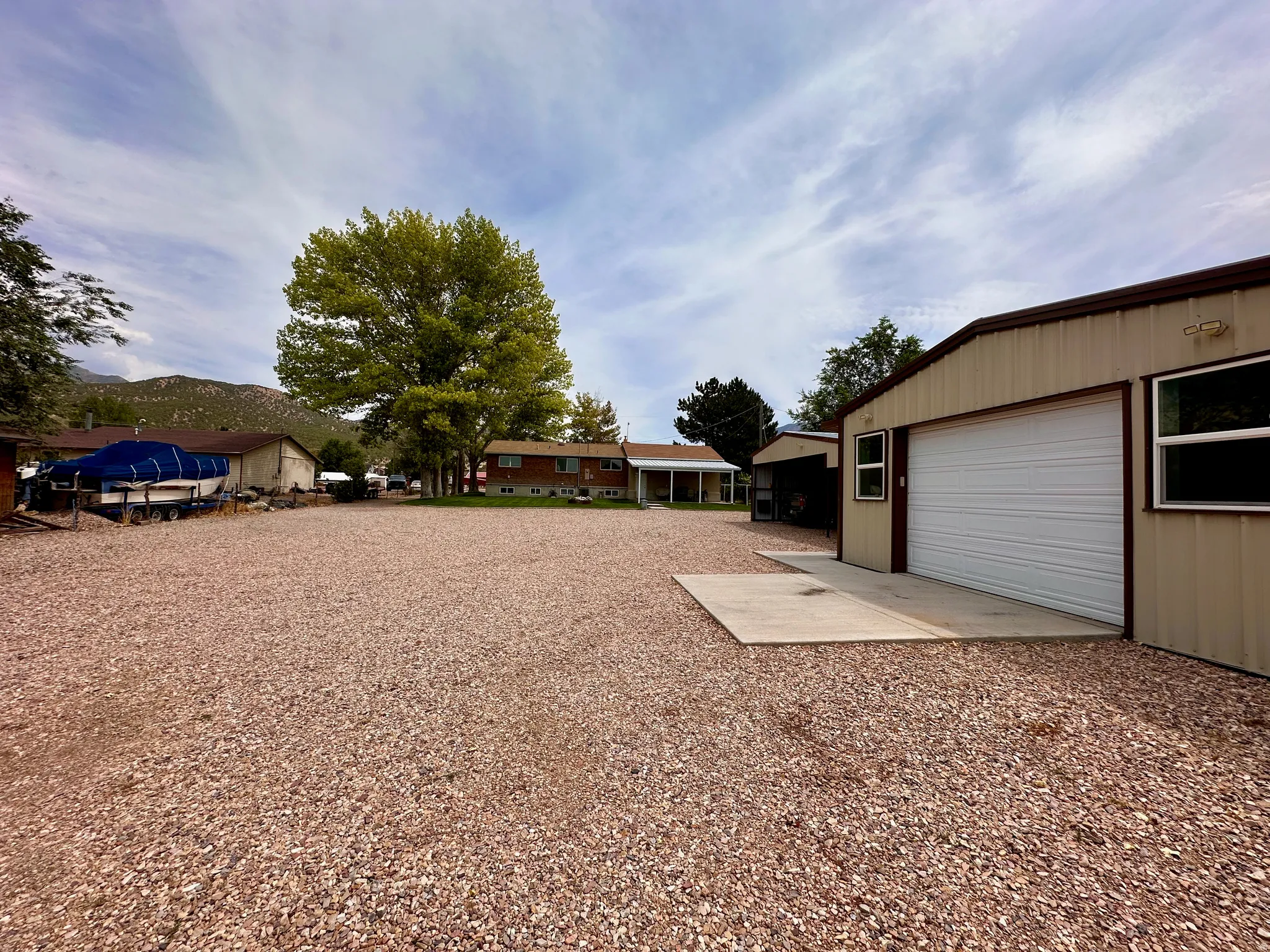 Gravel parking area, metal workshop with an automatic garage door, separate outbuilding, and mature trees