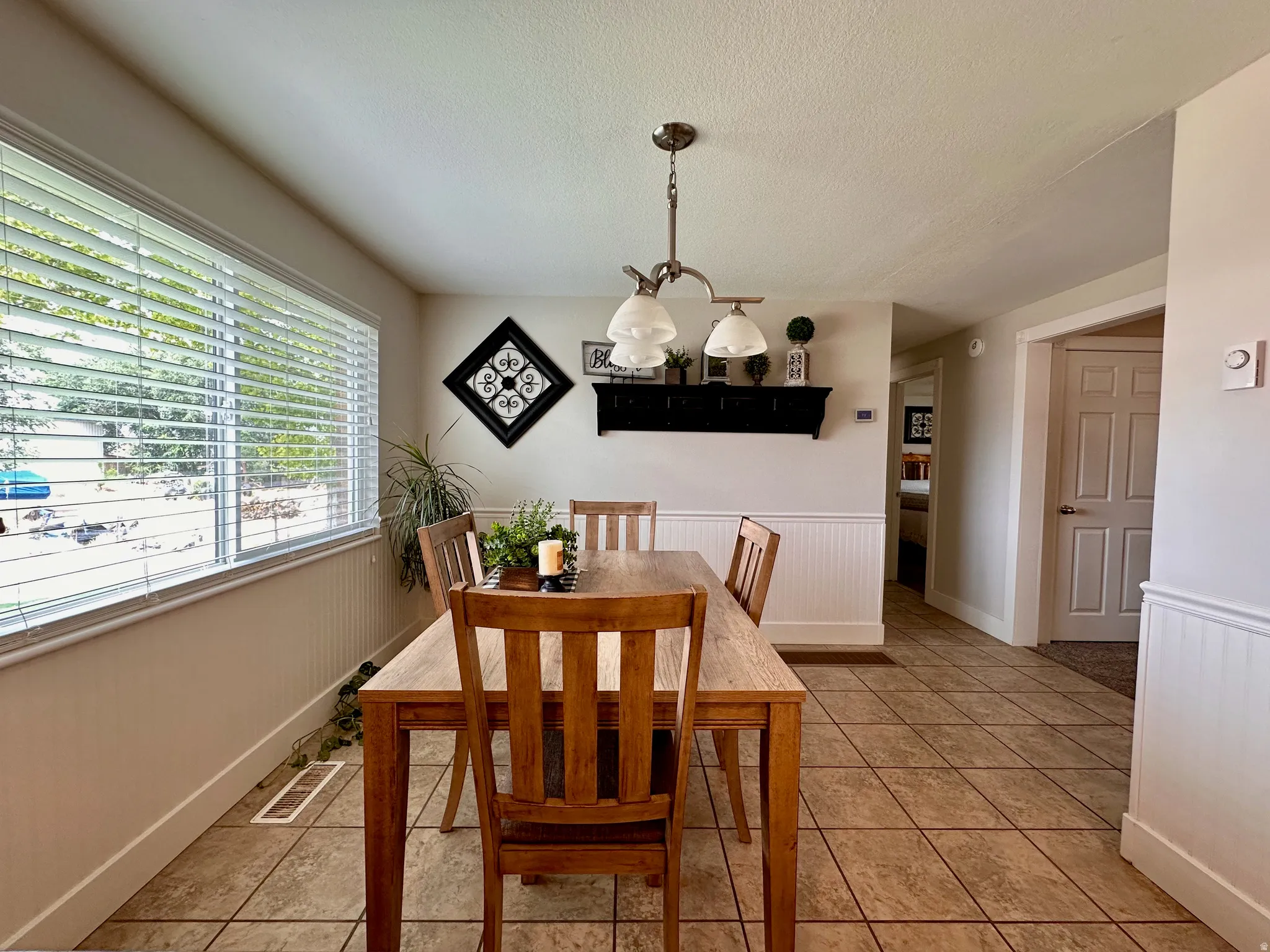 Tile flooring, window with blinds, decorative wainscoting, suspended ceiling light fixture, wall-mounted shelving