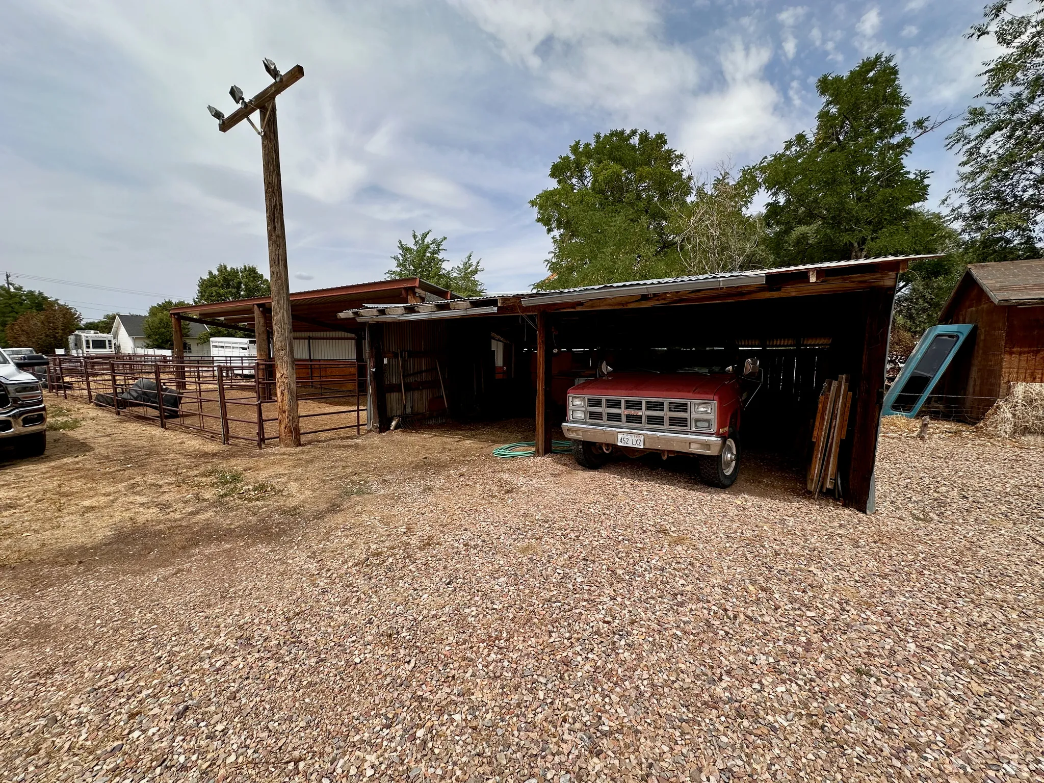 Gravel ground cover, open-sided shed structure, corrugated metal roof, fenced enclosure, utility pole