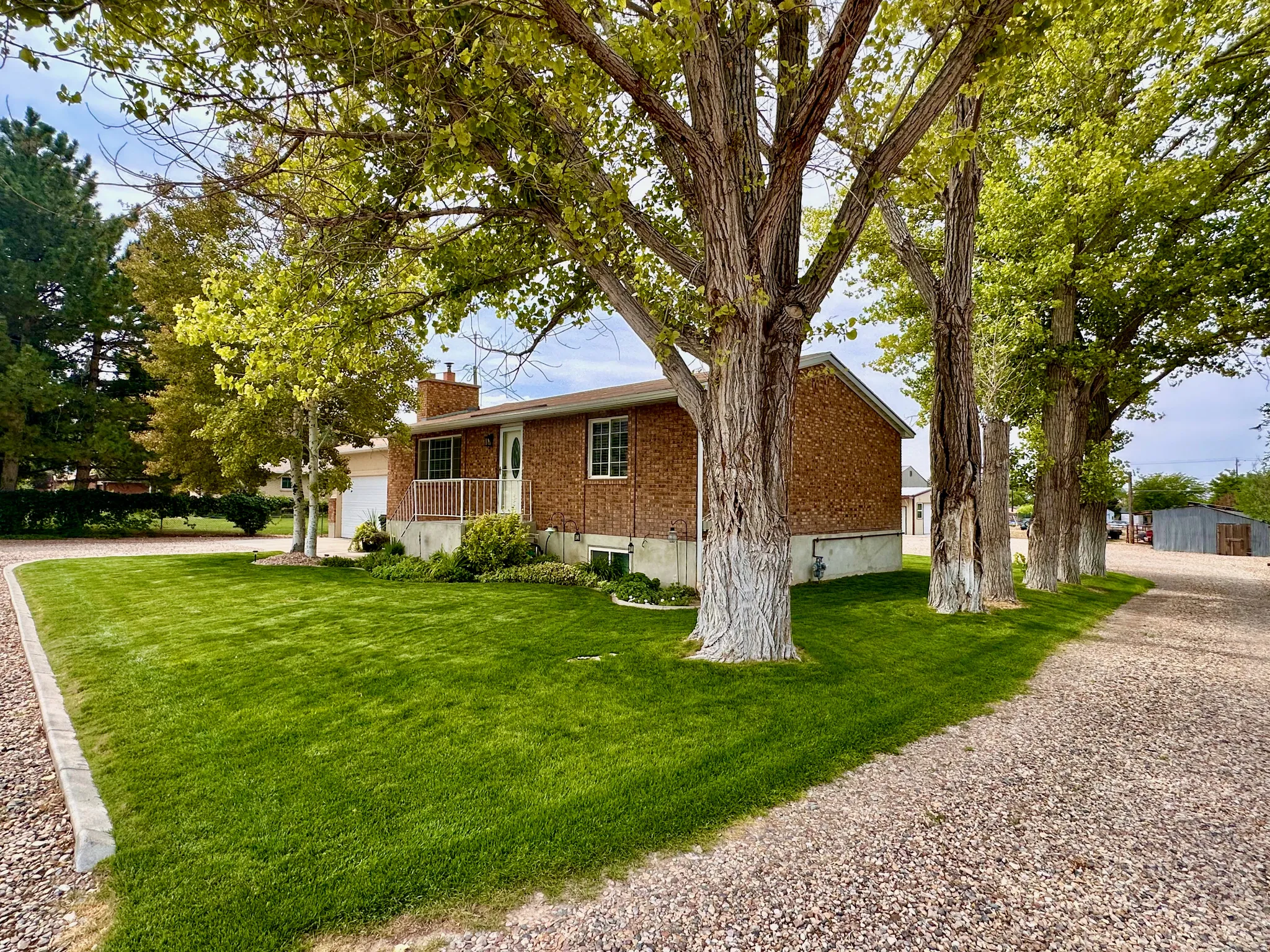 Brick exterior residence with a front porch and white railing, featuring a gravel driveway and an expansive lawn