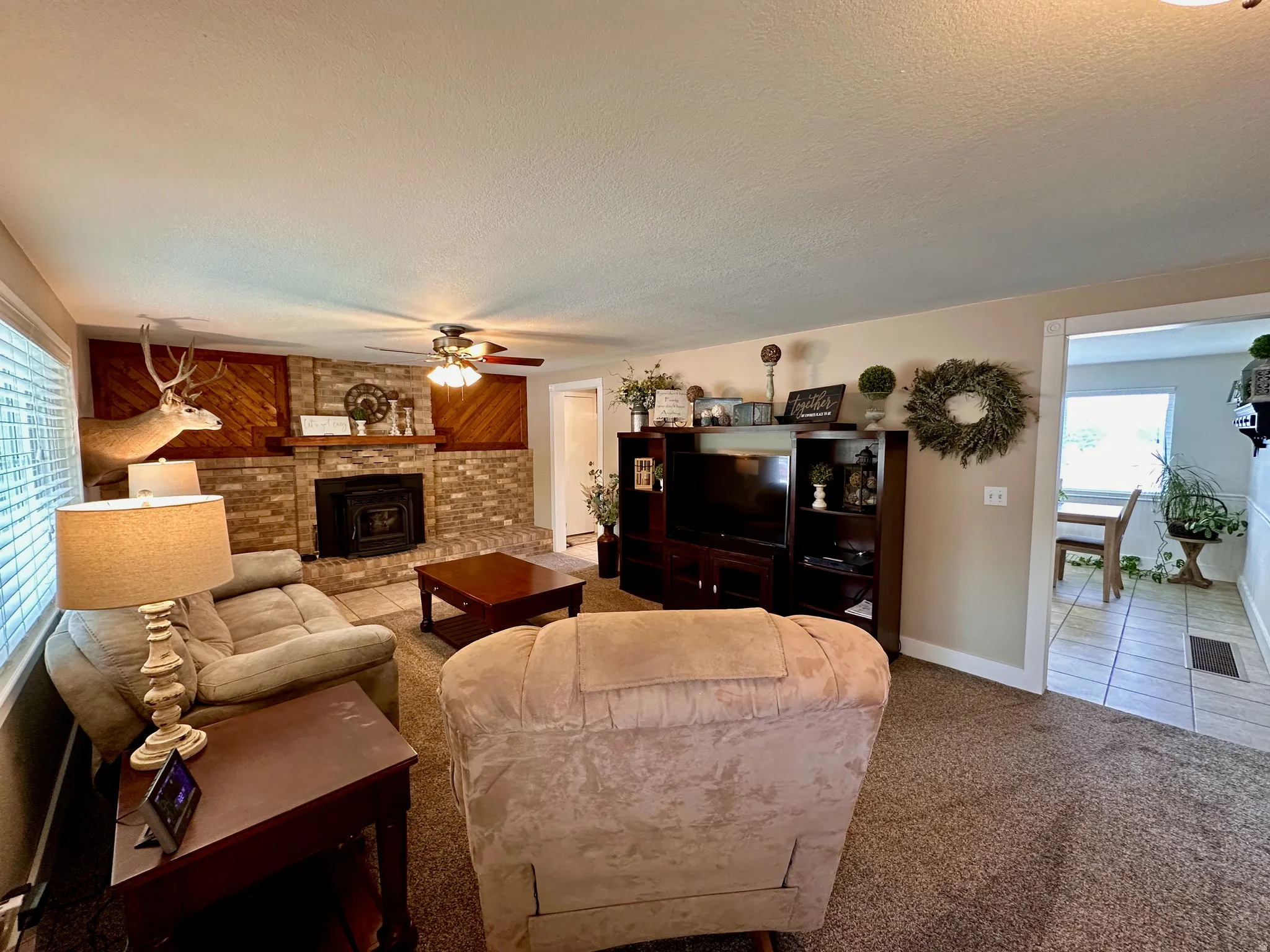 Living area with a stone-clad fireplace, wood panel accents, and a ceiling fan