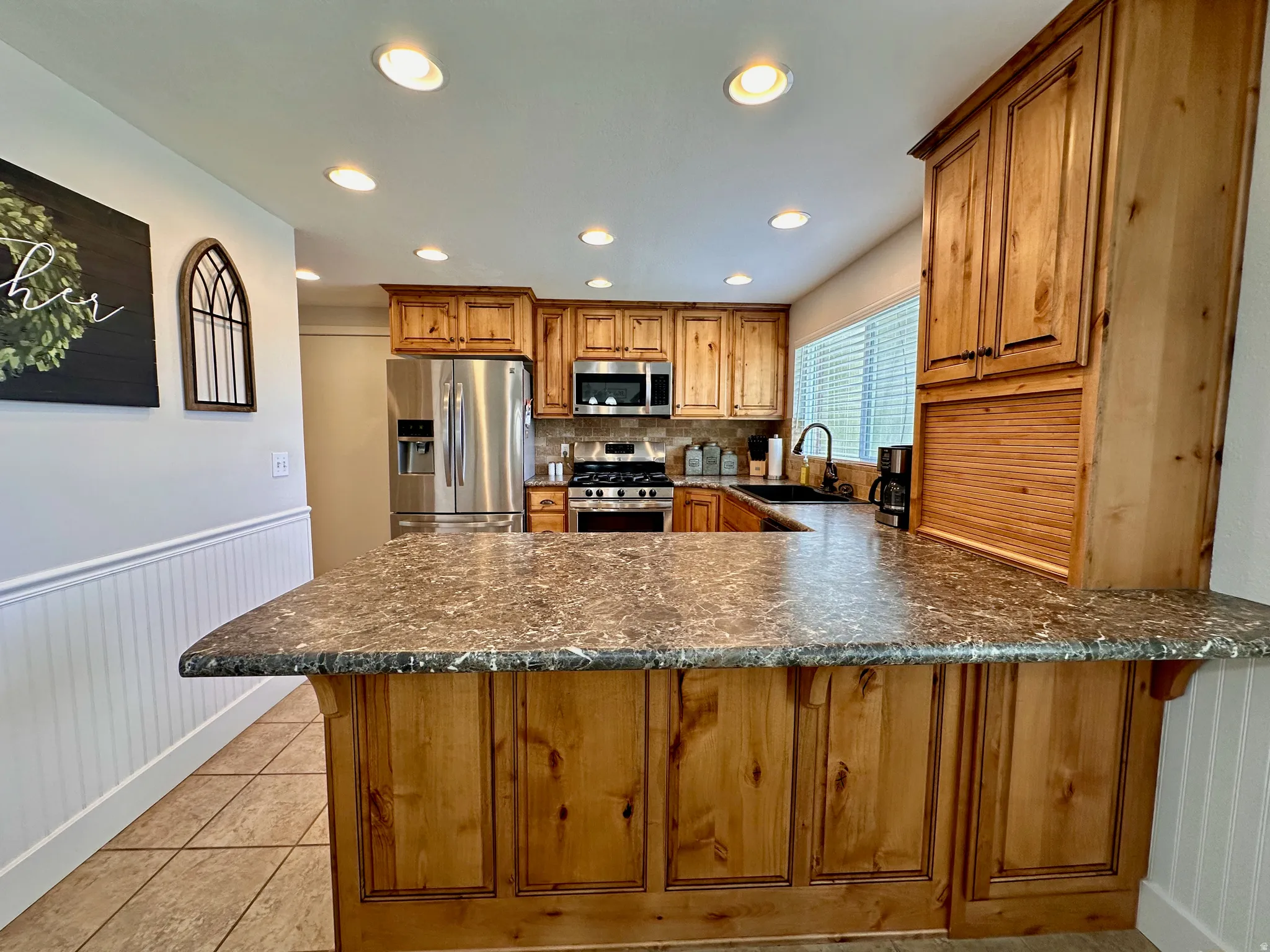 Kitchen featuring wood cabinetry, stainless steel appliances, recessed lighting, and a breakfast bar with a patterned countertop