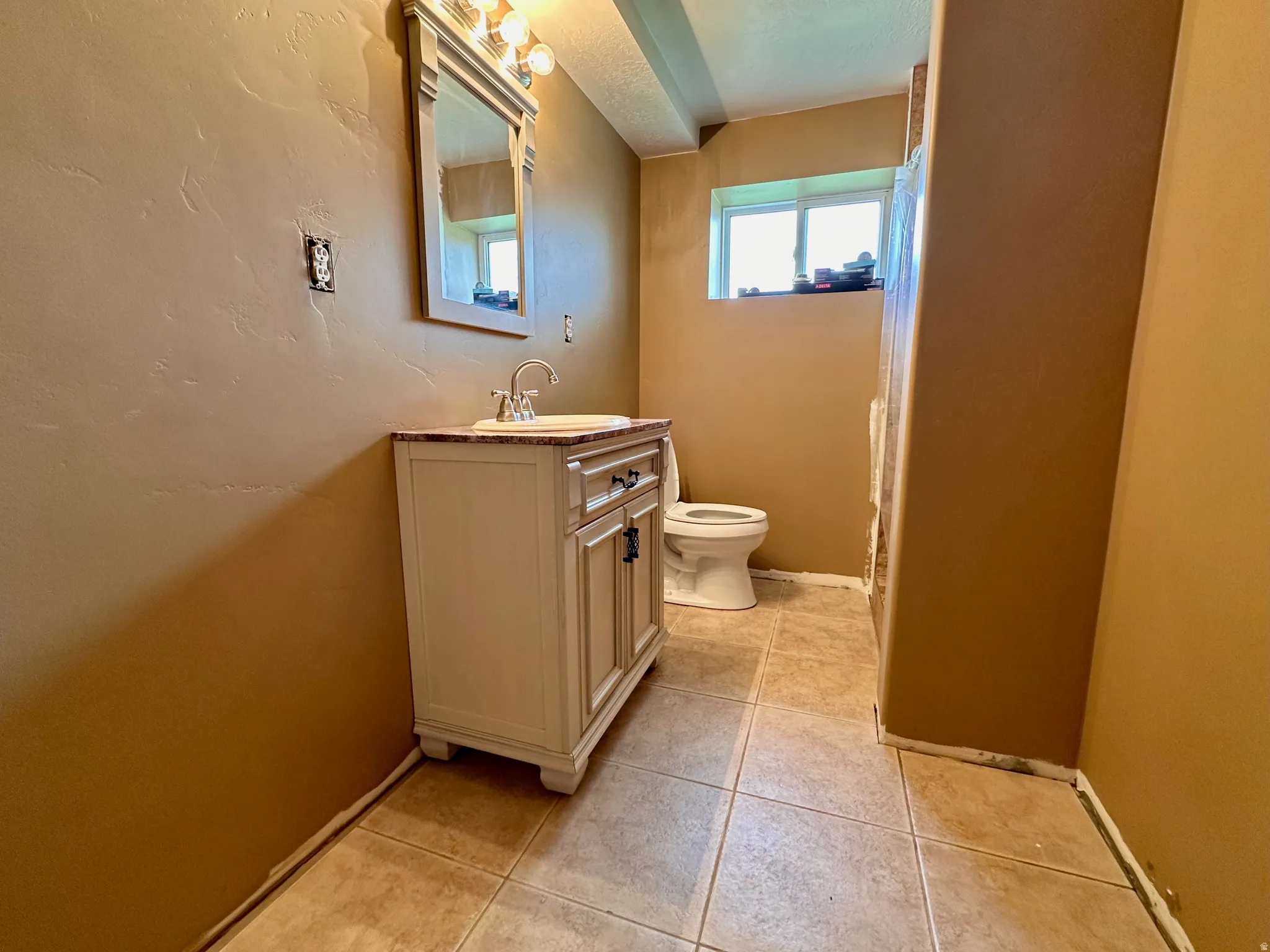 Light-toned tile flooring, vanity with a rectangular sink, wall-mounted mirror, and a window