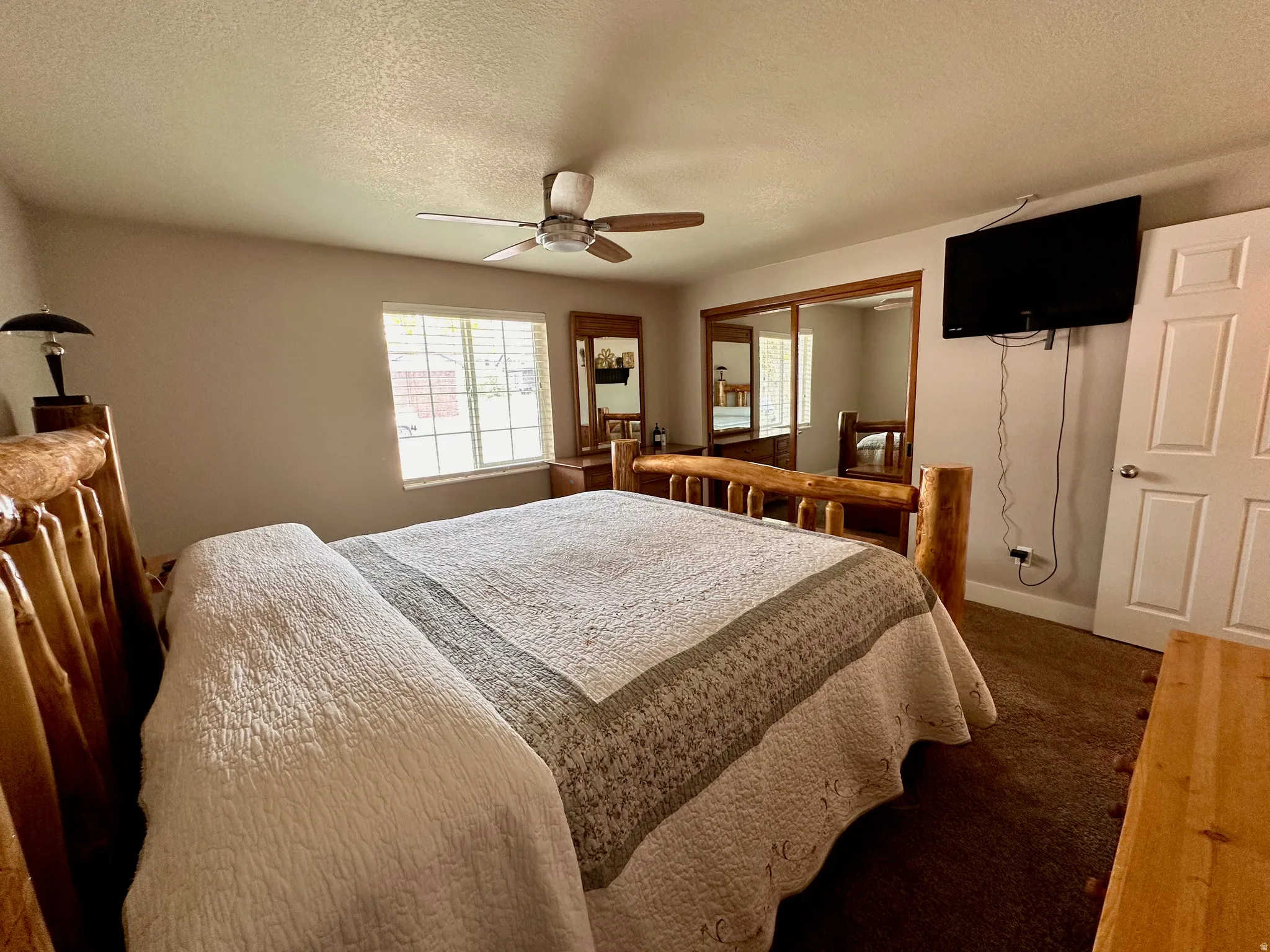Window with horizontal blinds, ceiling fan, mirrored closet doors, paneled interior door, and wall-mounted television