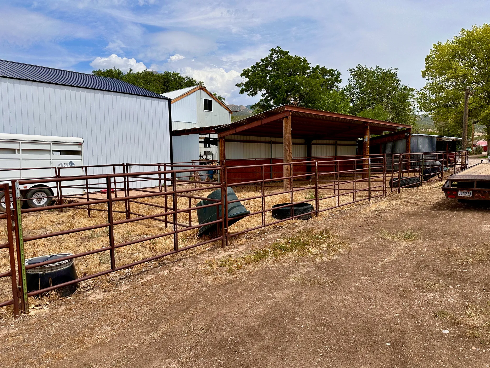 White metal barn with a black metal roof, featuring multiple fenced enclosures, covered stalls, and a secondary white building