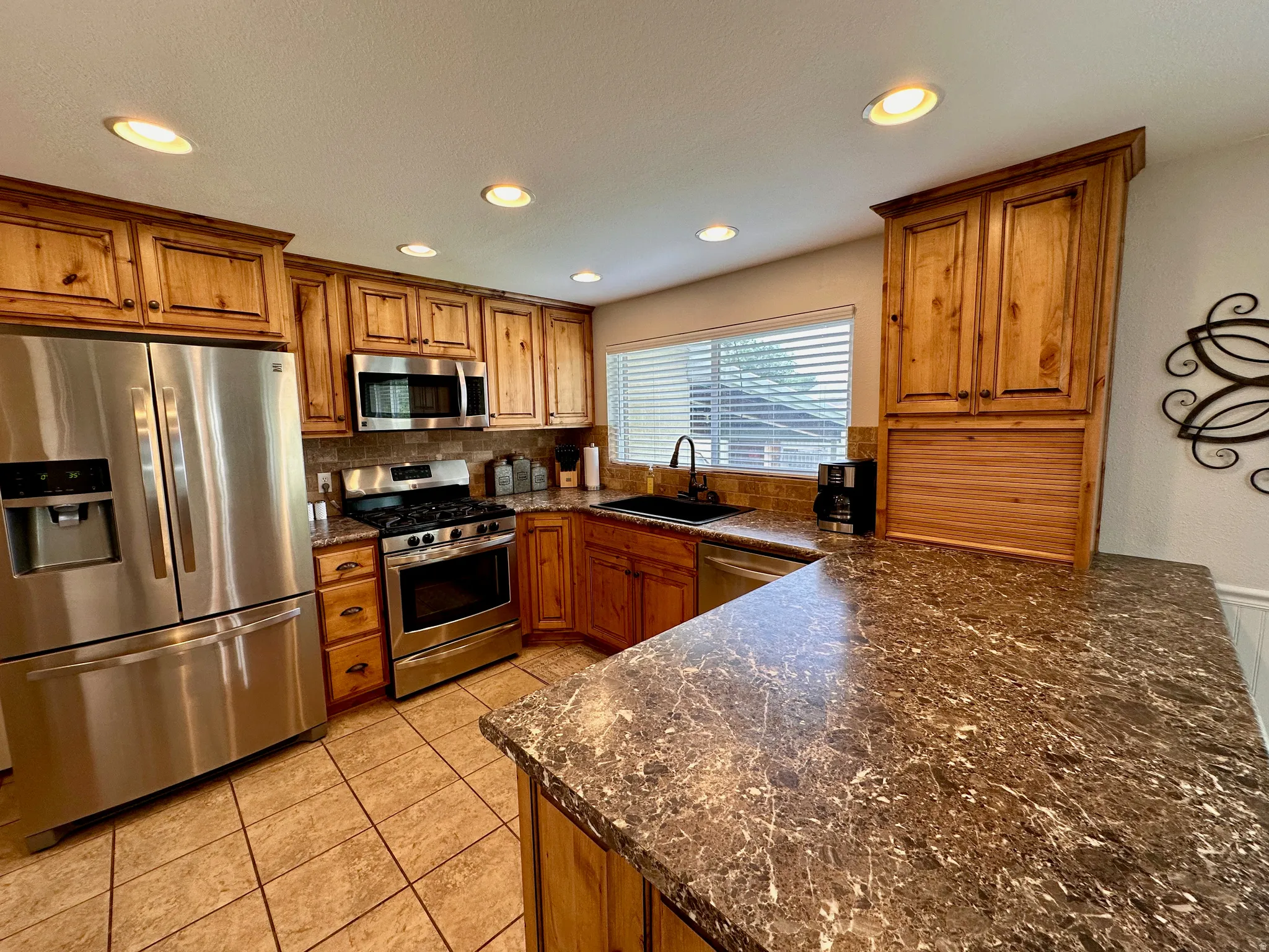 Kitchen featuring wood cabinetry, stainless steel appliances, recessed lighting, tile flooring, and a stone-finish countertop