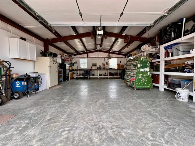 Expansive concrete floor in a workshop space, featuring exposed structural beams, white wall cabinetry, and built-in shelving units some  will stay, west wall of shelving is not included.  also the metal cover over the work bench will not stay.  It will b