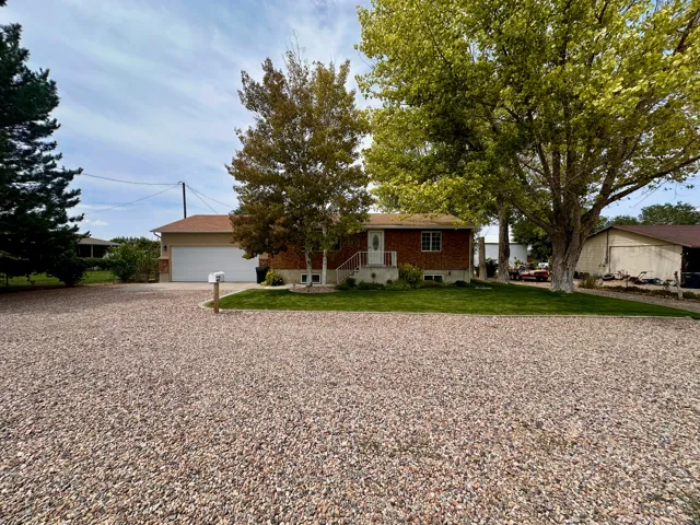 Brick facade, white garage door, gravel driveway, mature trees, manicured lawn