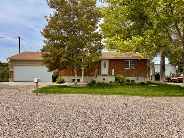 Brick exterior with white trim, attached garage, gravel driveway, mature trees, and a manicured lawn