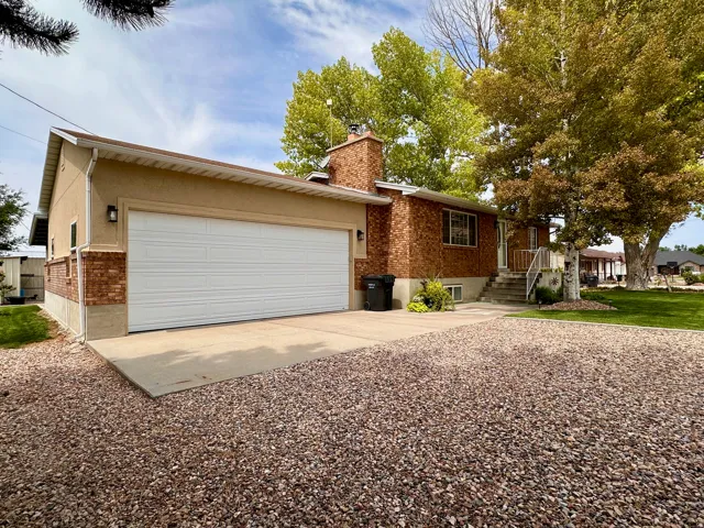Brick and stucco exterior, attached garage, concrete driveway, gravel landscaping, mature trees