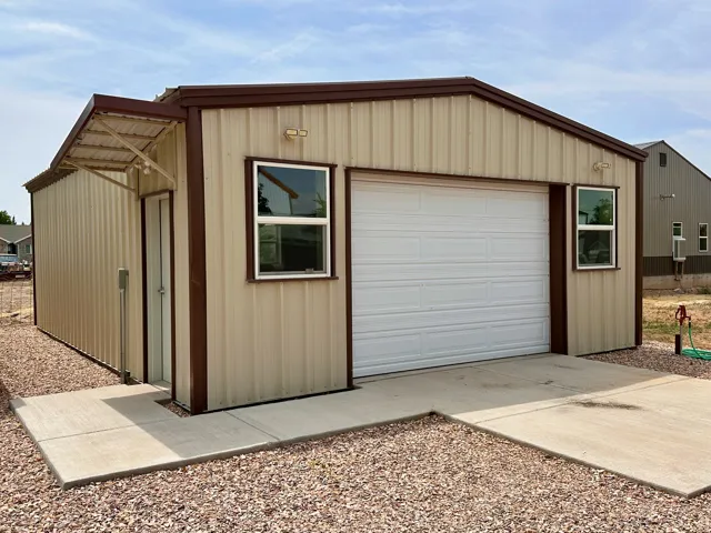 Metal-sided structure with a single garage door, two windows, and an awning over a side entrance