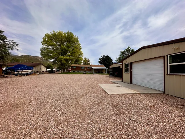 Gravel parking area, metal workshop with an automatic garage door, separate outbuilding, and mature trees