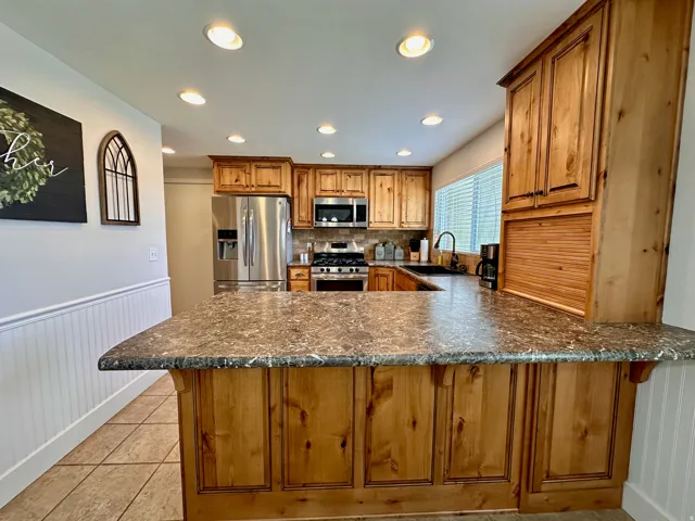 Kitchen featuring wood cabinetry, stainless steel appliances, recessed lighting, and a breakfast bar with a patterned countertop