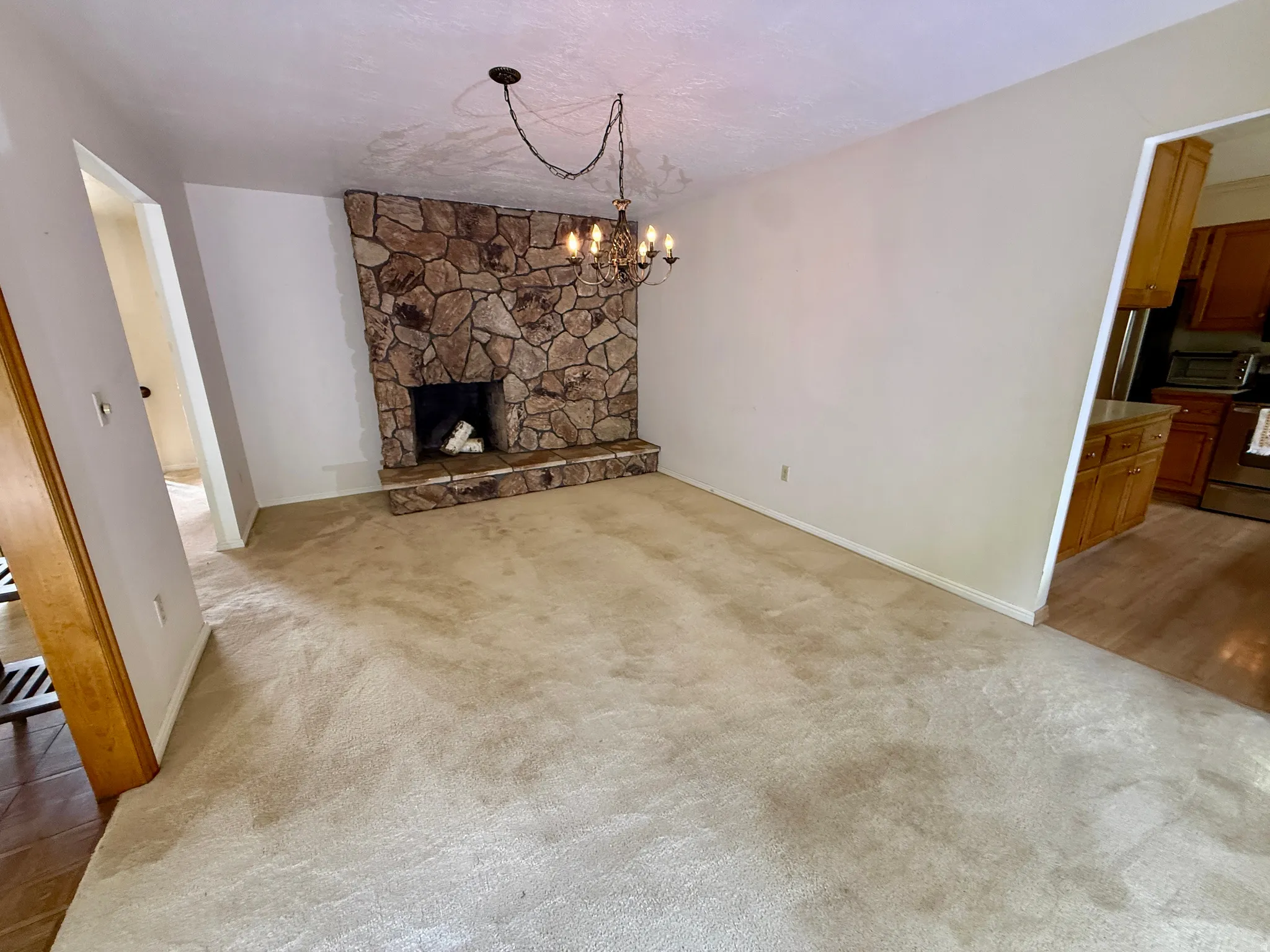 Stone-clad fireplace with hearth, overhead chandelier, and carpeted flooring
