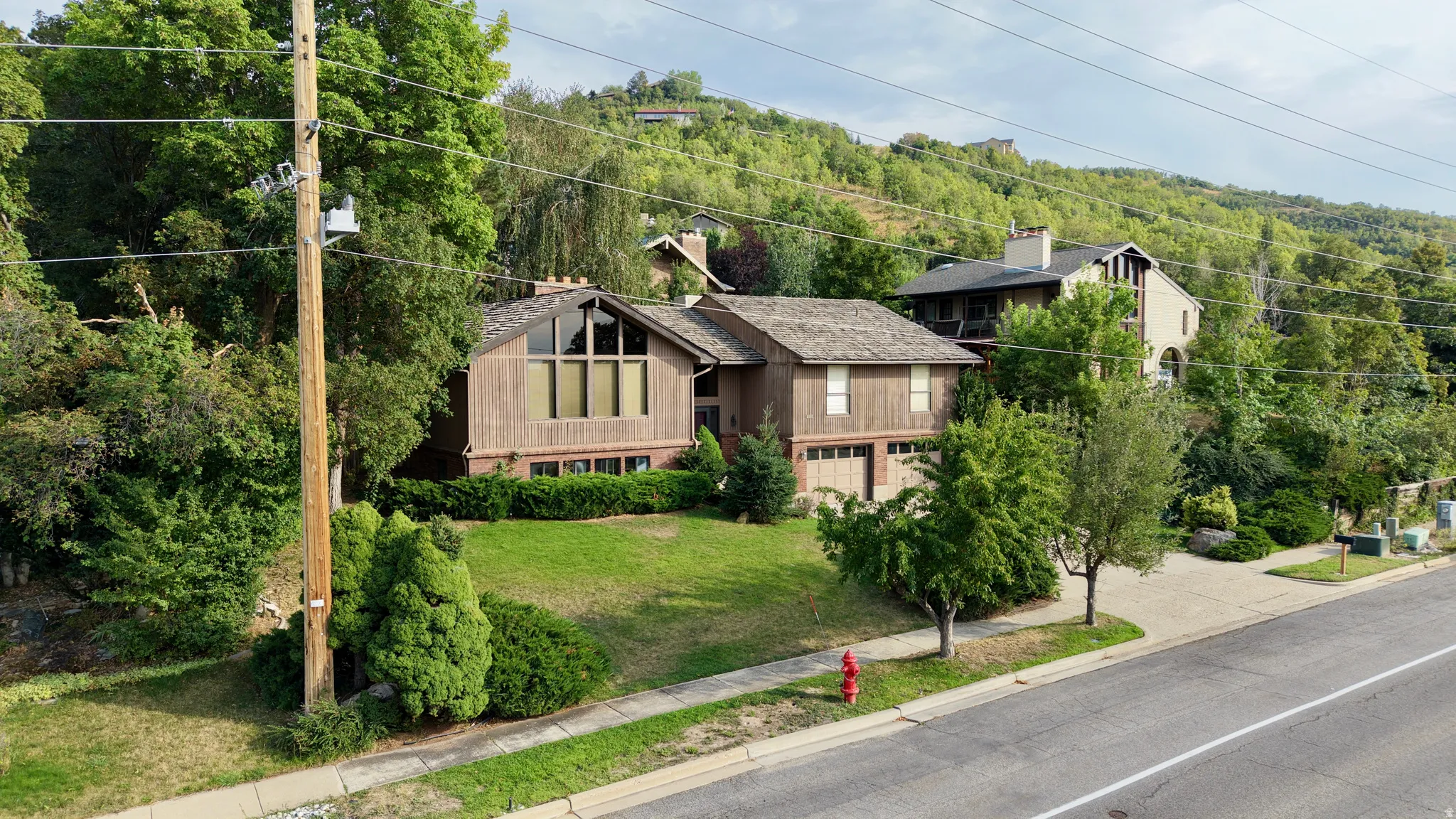 Brown wood-sided exterior with a large picture window, shingle roof, and attached garage