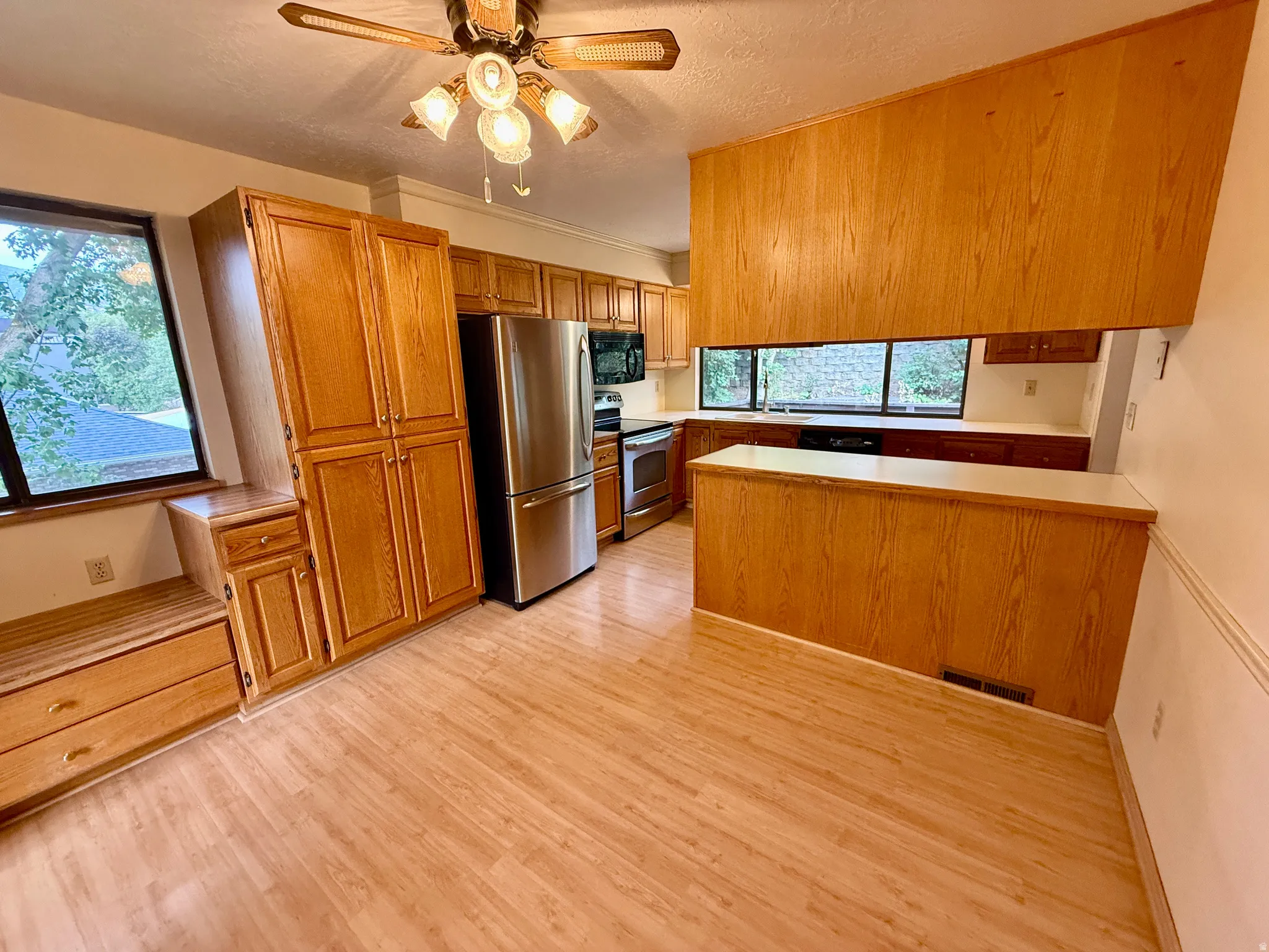 Kitchen featuring wood-finish flooring, wood cabinetry, stainless steel appliances, and a ceiling fan with integrated lighting