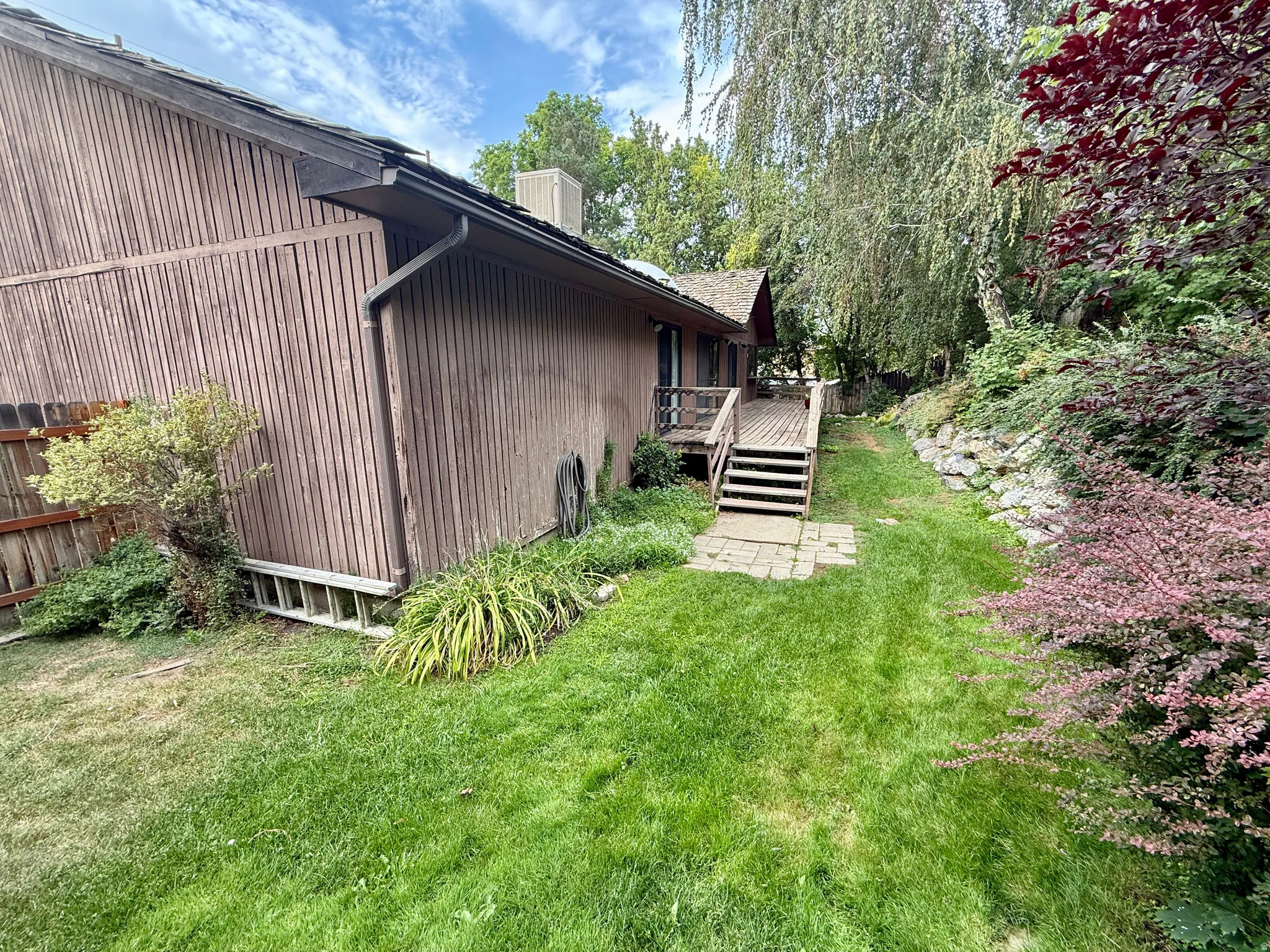 Exterior featuring vertical wood siding, a wood deck with stairs, and a retaining wall